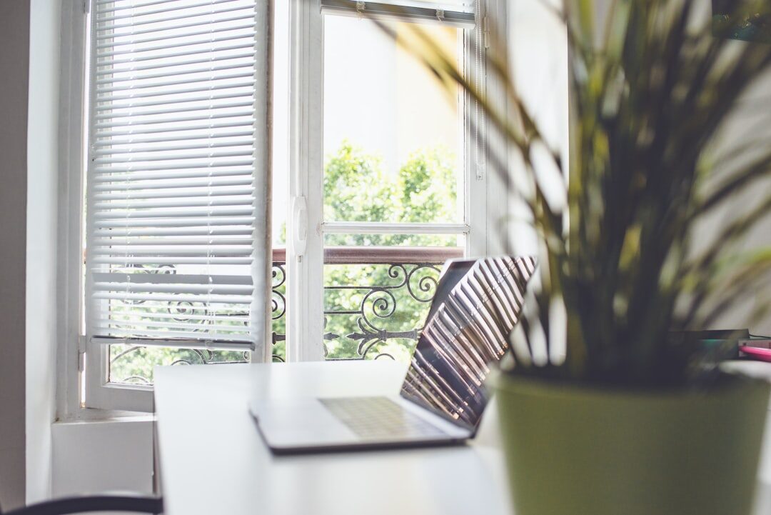 Bright modern office desk with a laptop and notebook near a window