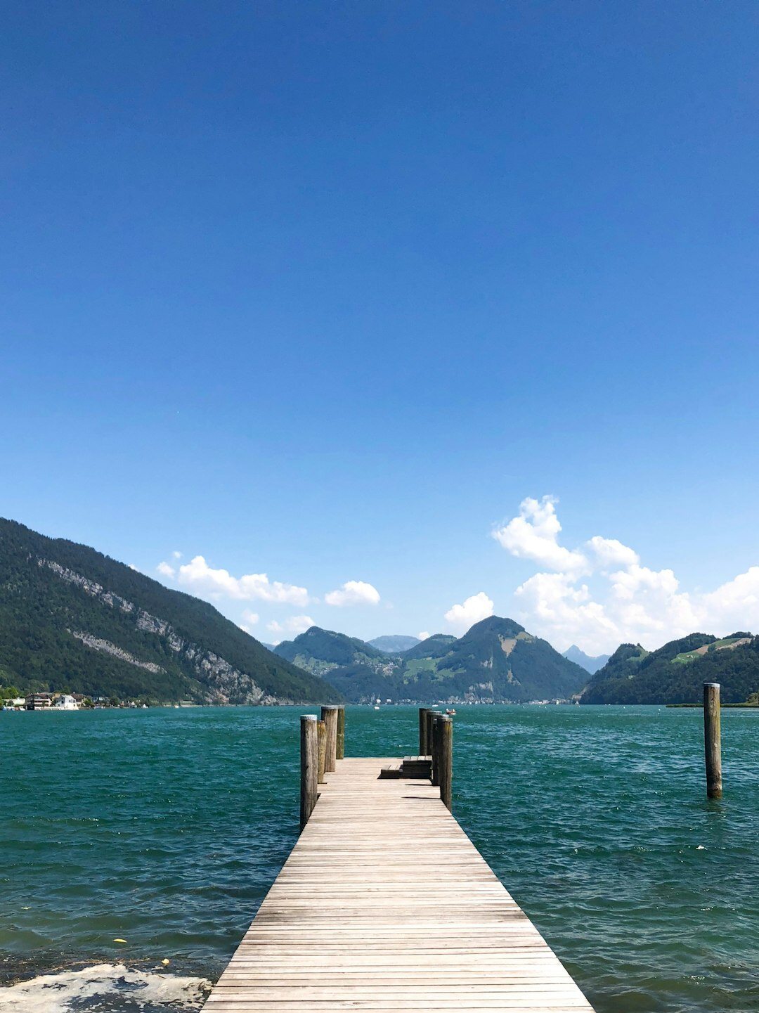 Wooden dock extending into a clear blue Swiss lake surrounded by mountains